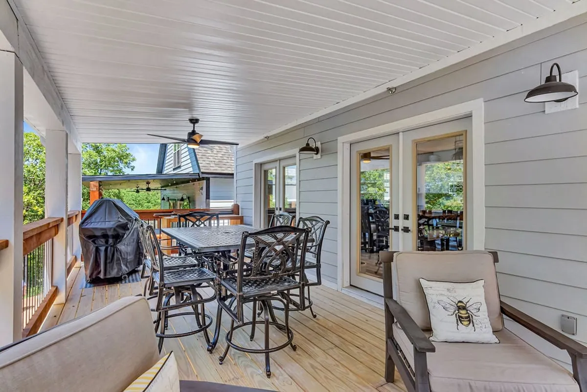 An inviting outdoor dining area featuring a spacious table, comfortable seating, and a grill set up on a screened-in deck. The space is surrounded by greenery and appears ideal for relaxed social gatherings or sunset dinners, with a Webber BBQ grill ready for use.