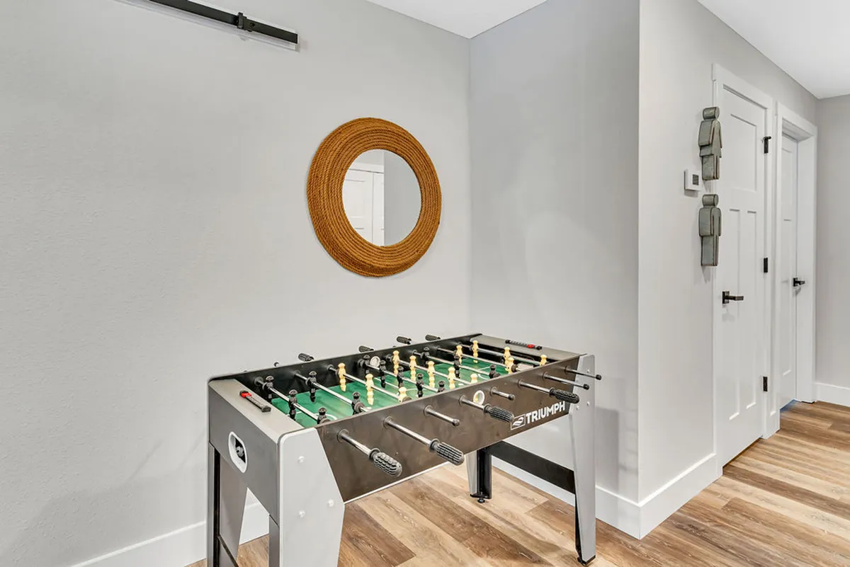 A vibrant interior scene featuring a foosball table prominently, with a circular mirror and wooden accents. The room feels lively and inviting, suggesting active play and cheerful socializing.
