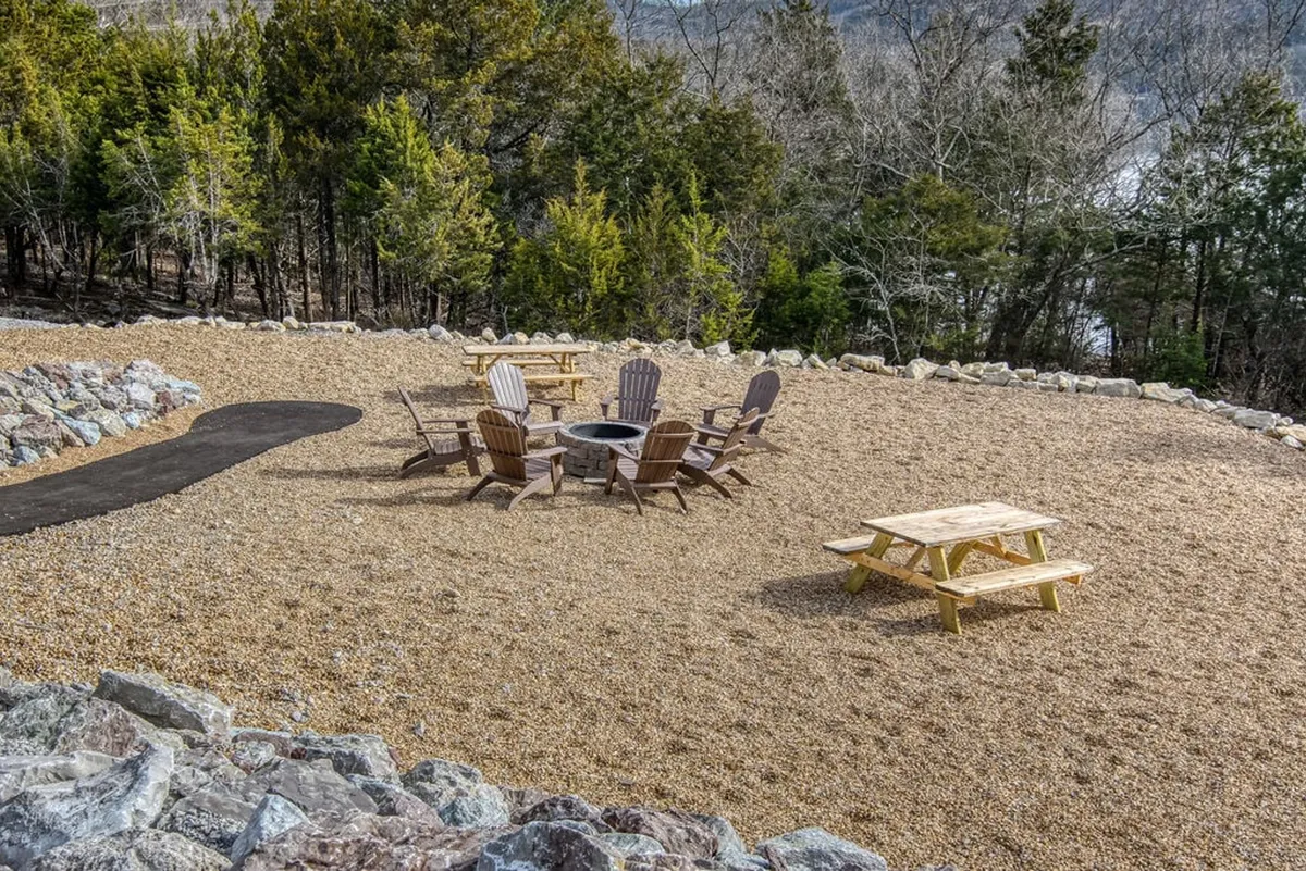 A cozy fire pit area surrounded by Adirondack chairs, set against a backdrop of trees and open sky. The space includes a picnic table, making it ideal for social gatherings, s’mores, and evening relaxation after a day on the lake.