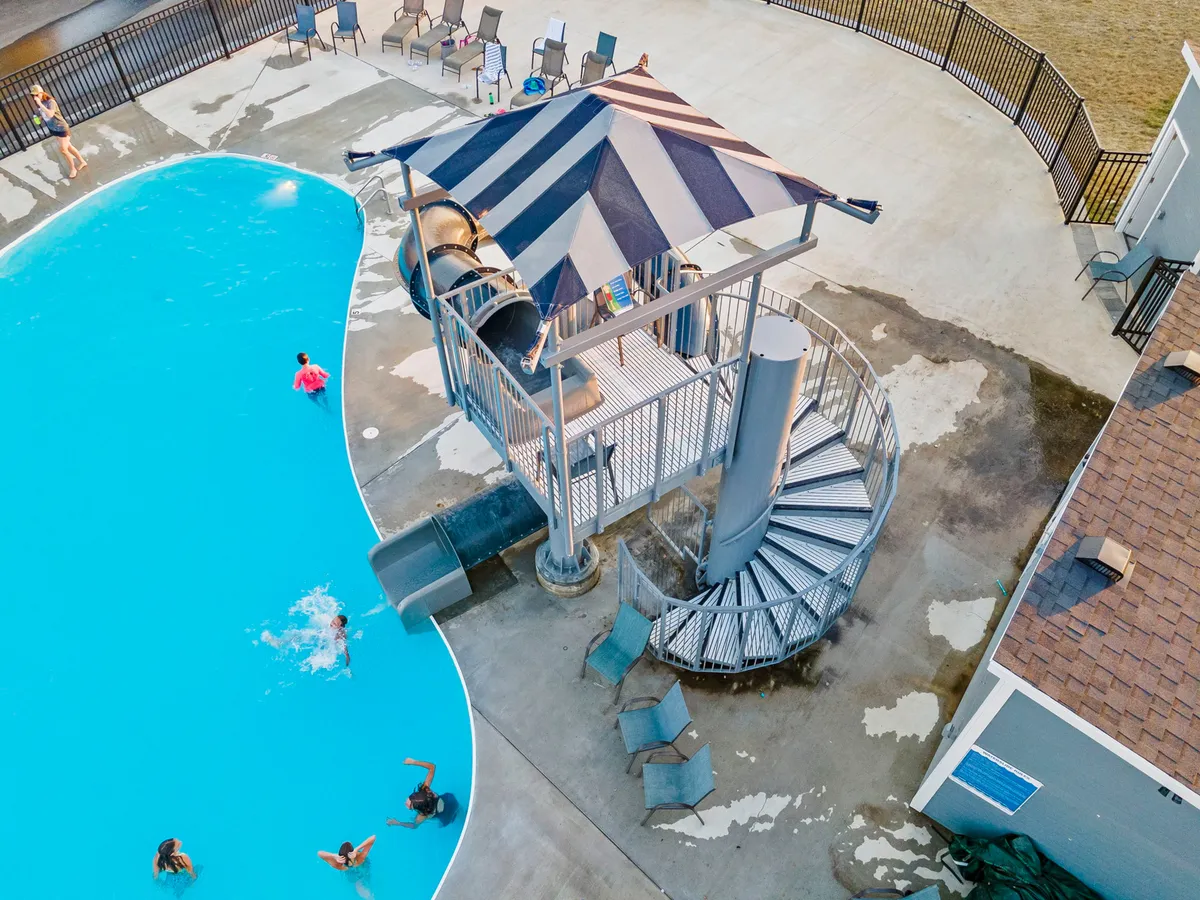 This image captures a vibrant outdoor scene featuring a swimming pool with a water slide and several deck chairs, all bathed in sunlight. The area is designed for both fun and relaxation, hinting at lively summer days spent swimming, sliding, and soaking up the sun.