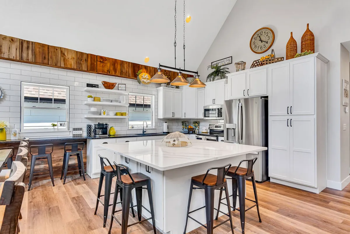 The image showcases a spacious, light-filled kitchen with a large central island, sleek modern appliances, elegant pendant lighting, and warm wooden accents. The open layout creates an inviting atmosphere, perfect for cooking, gathering, and making memories with family and friends.
