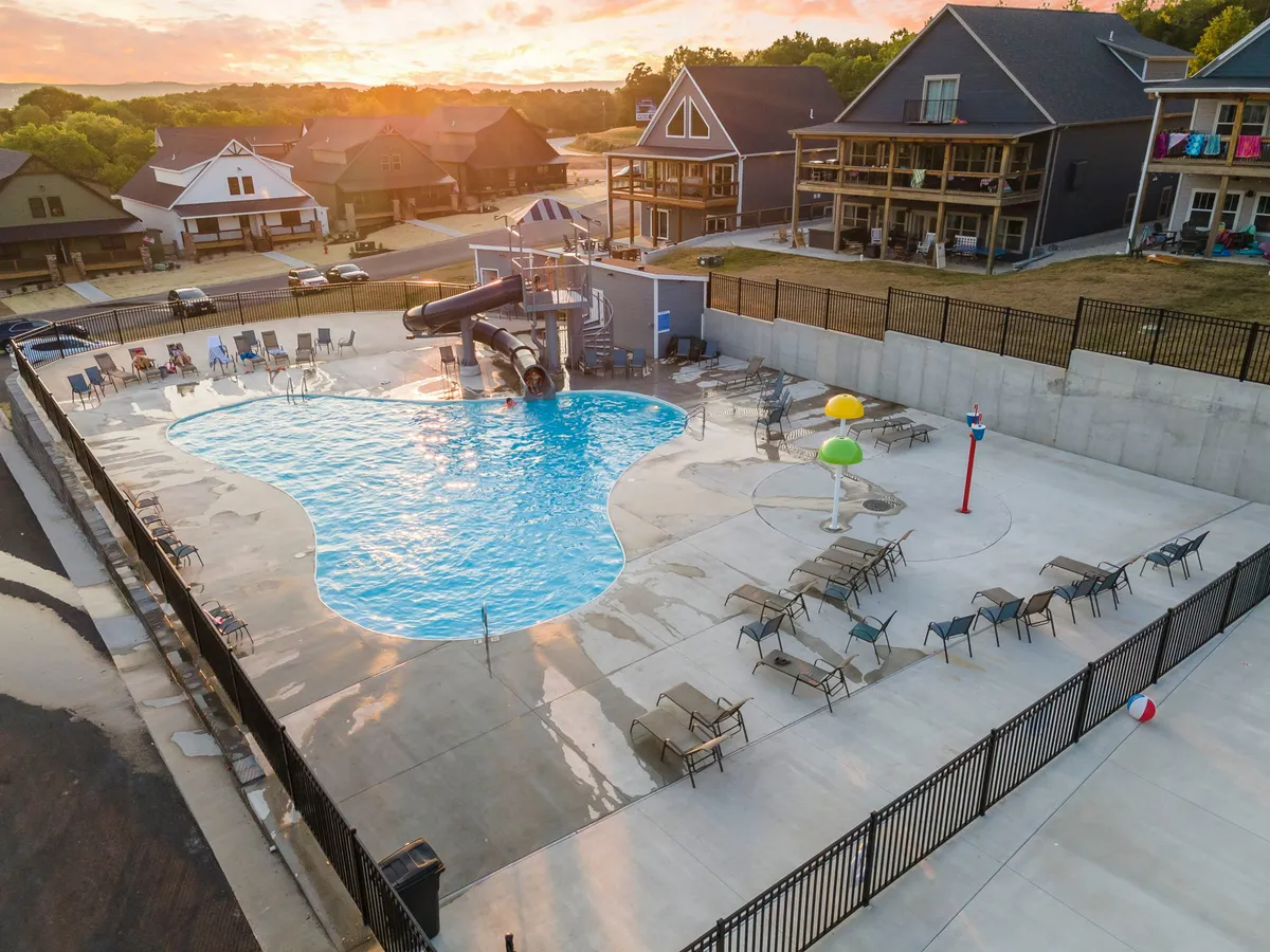 A vibrant exterior shot featuring the resort's swimming pool, complete with a water slide, lounge chairs, and colorful water features. The playful design and inviting water make it ideal for family gatherings and children's fun. The overall mood is energetic and relaxed, capturing the essence of summer excitement and recreation.