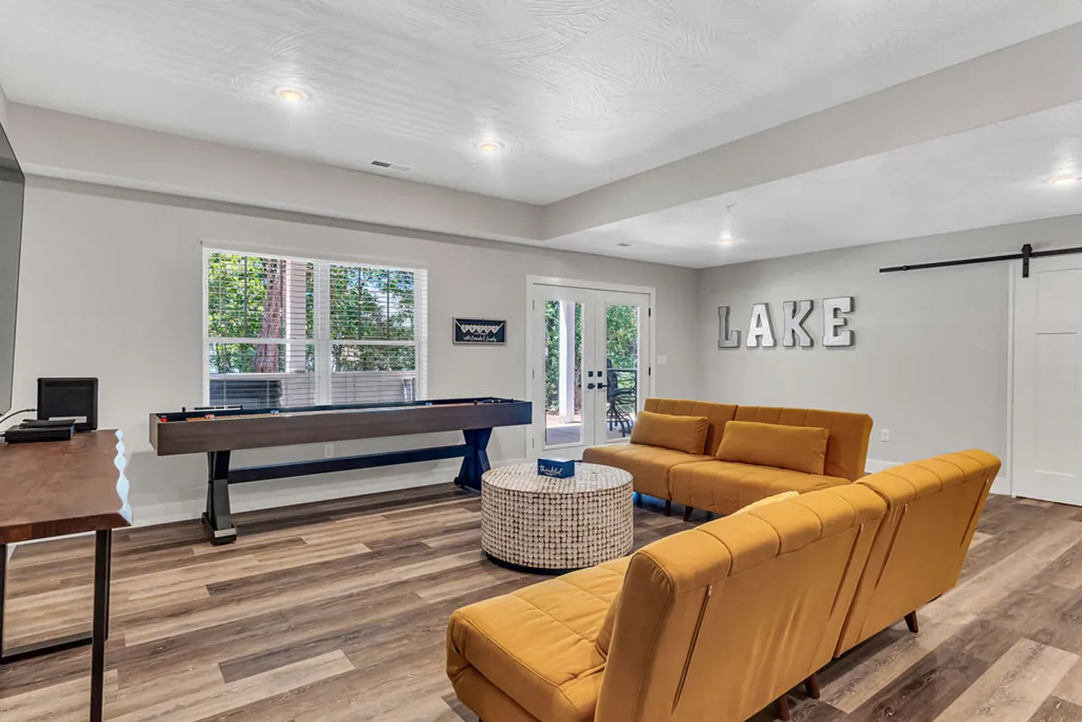 A playful entertainment lounge is depicted, featuring a bright yellow sofa, a pool table, 'LAKE' wall art, and a round coffee table. The room feels lively and designed for engaging in games, socializing, and making memories.