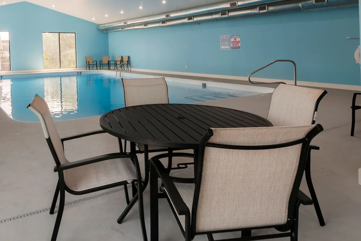 A sunlit indoor swimming pool with a round table and chairs beside large windows, blending relaxation and activity. The inviting pool area is ideal for year-round swimming and provides a luxurious, resort-style amenity for guests.