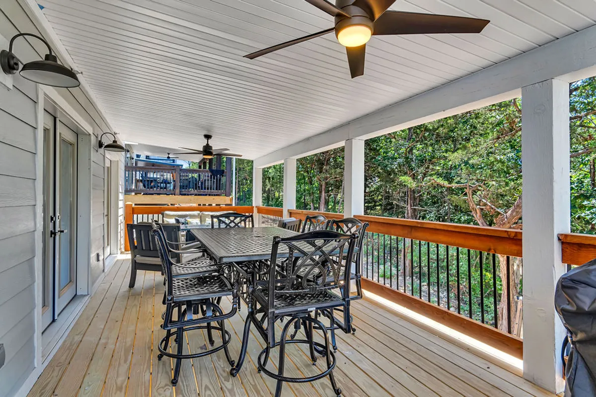 An inviting screened-in deck with a dining table, overhead fans, wooden railing, and views of lush greenery. The space is furnished for outdoor dining and relaxing, making it an ideal extension of the kitchen for indoor-outdoor entertaining.