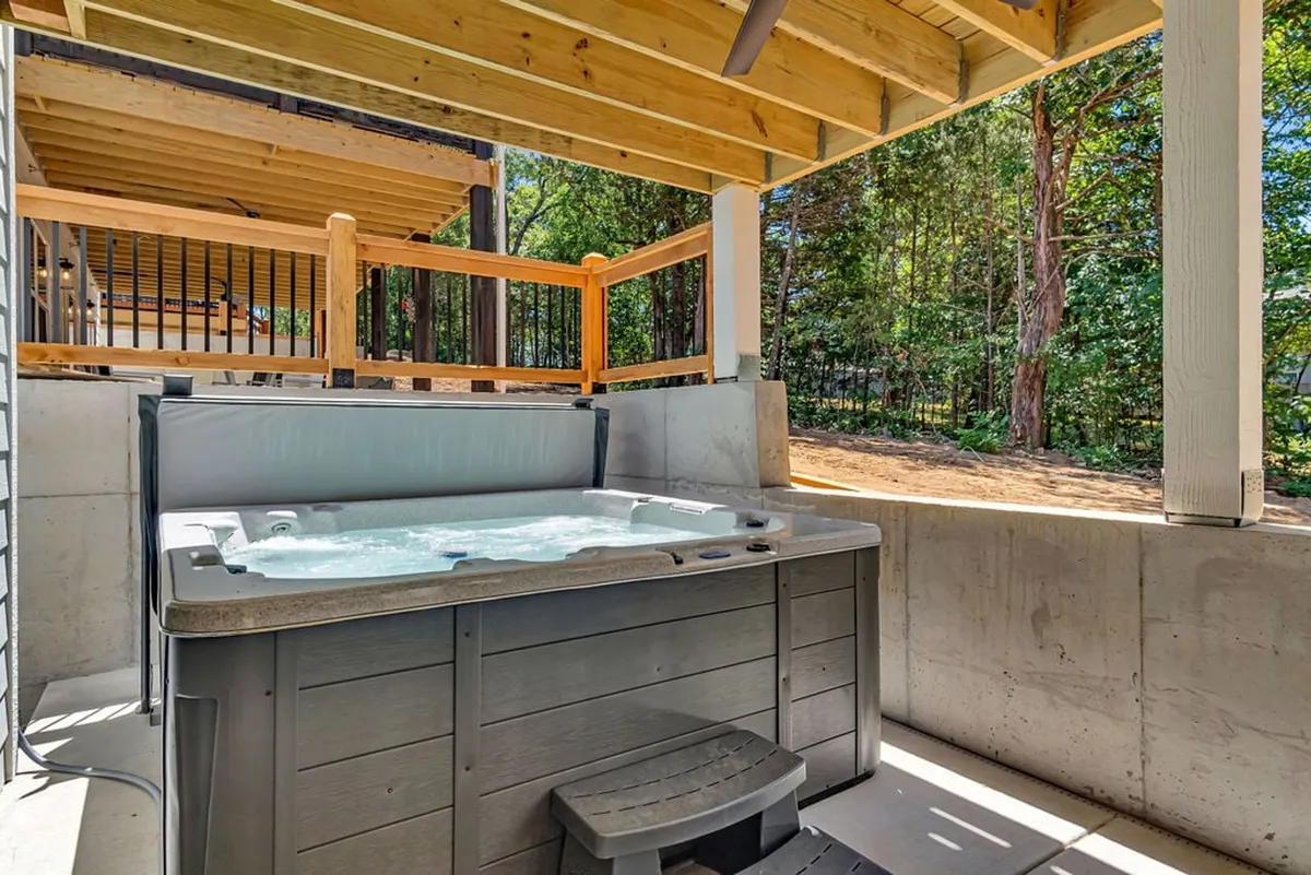 An inviting exterior deck area with a bubbling hot tub surrounded by trees. The tranquil, covered space is ideal for unwinding after competitive games, offering relaxation rain or shine.