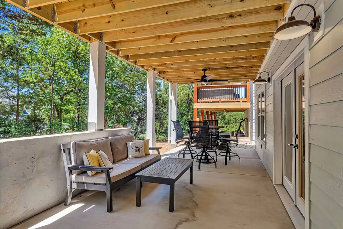 An exterior outdoor living area with a sofa, outdoor dining set, and a wooden ceiling structure, surrounded by greenery. The space is perfect for enjoying meals, relaxing, or unwinding outside with pets in a secure, comfortable environment.