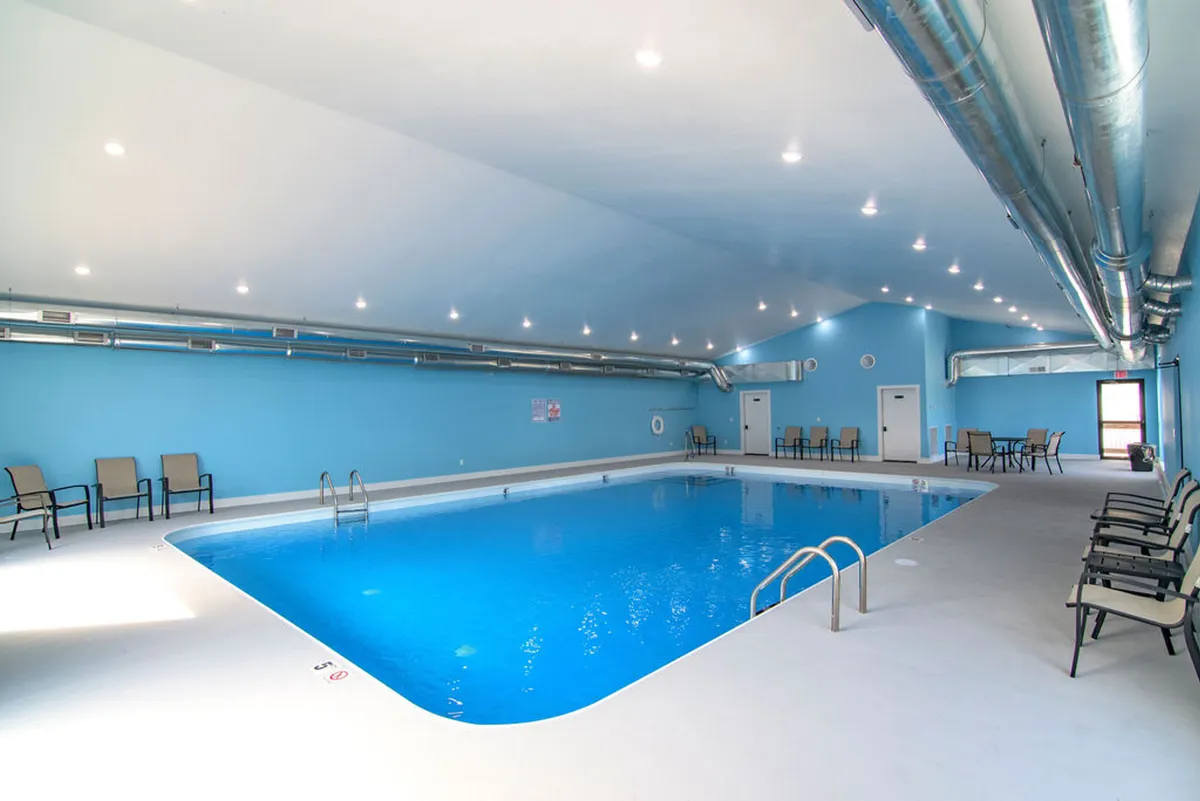 An inviting indoor pool scene is shown, complete with calm blue walls, lounge chairs, and soft lighting. The tranquil atmosphere suggests year-round swimming and relaxation, regardless of the weather outside.