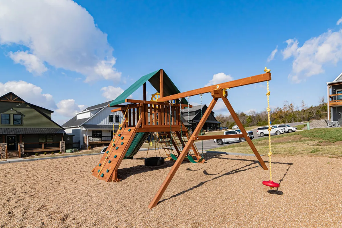 An exterior image of a cheerful playground structure surrounded by sand and swings, set in a sunny, open area. Children are shown playing, suggesting the space is lively and perfect for energetic family outings. The playground stands out as a joyful, community-focused feature.