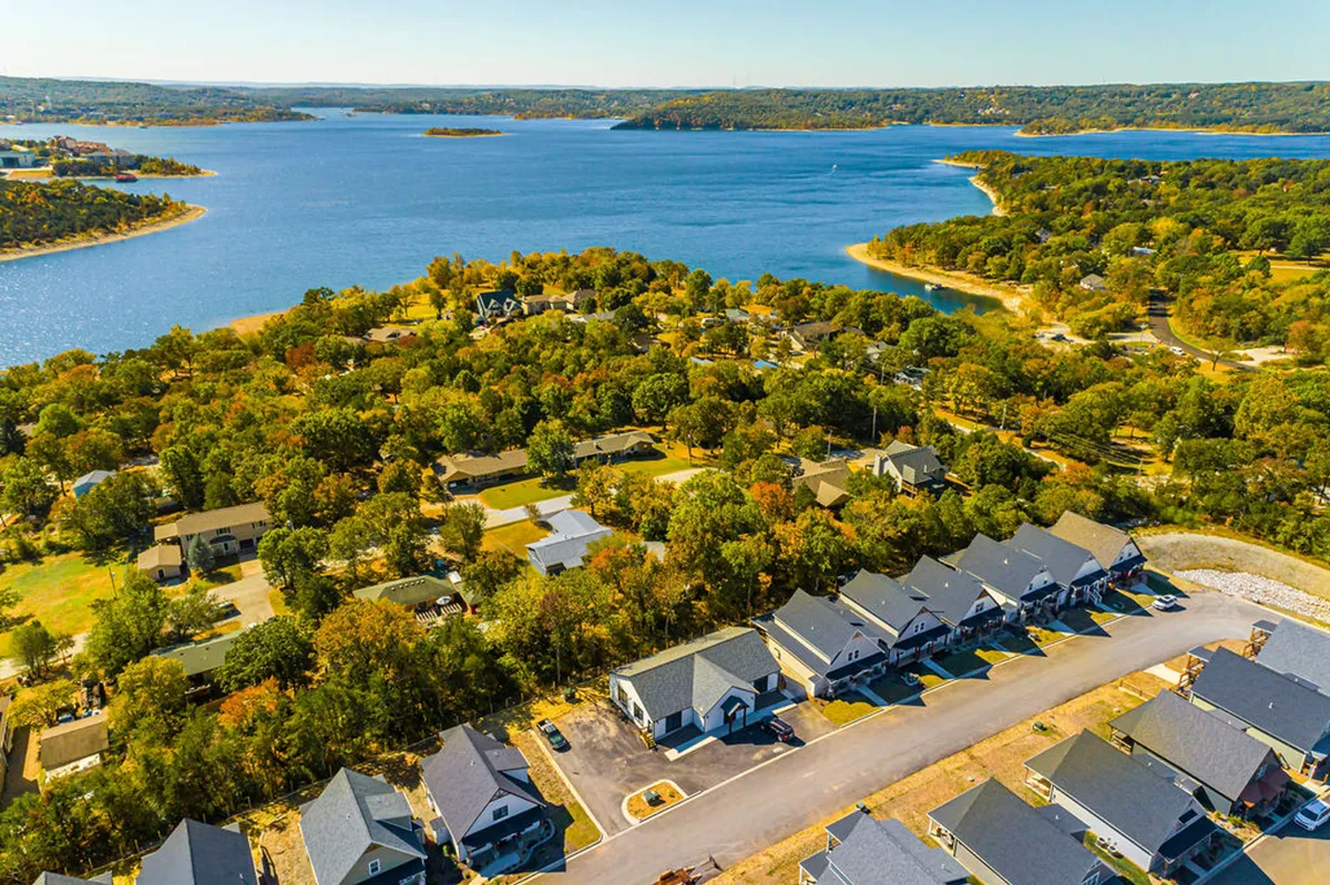 A wide, tranquil view of Table Rock Lake framed by lush greenery and neighborhood homes. The calm water and open sky invite thoughts of lake activities such as paddleboarding, fishing, and boating. The surrounding landscape emphasizes the property’s proximity to recreational opportunities.