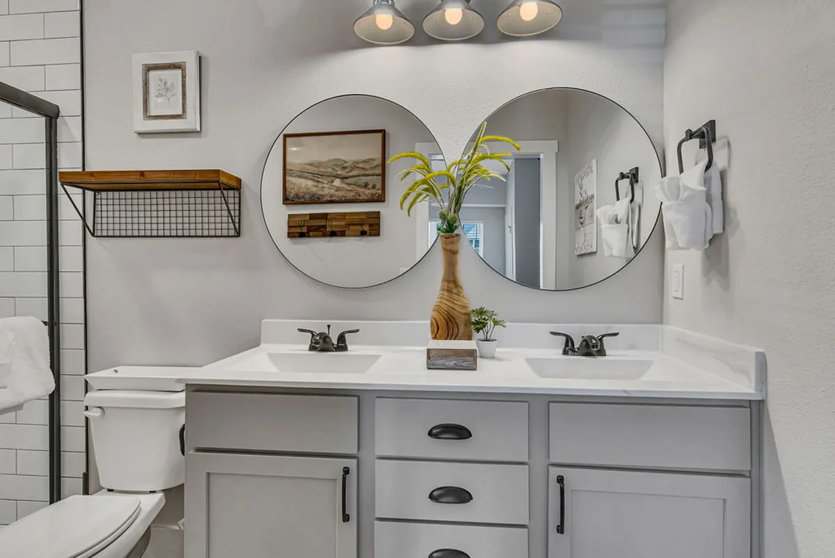 A modern bathroom with double vanity mirrors, sleek wooden shelving adorned with towels and decor, and contemporary light fixtures. The atmosphere is refreshing and inviting, ideal for unwinding routines.